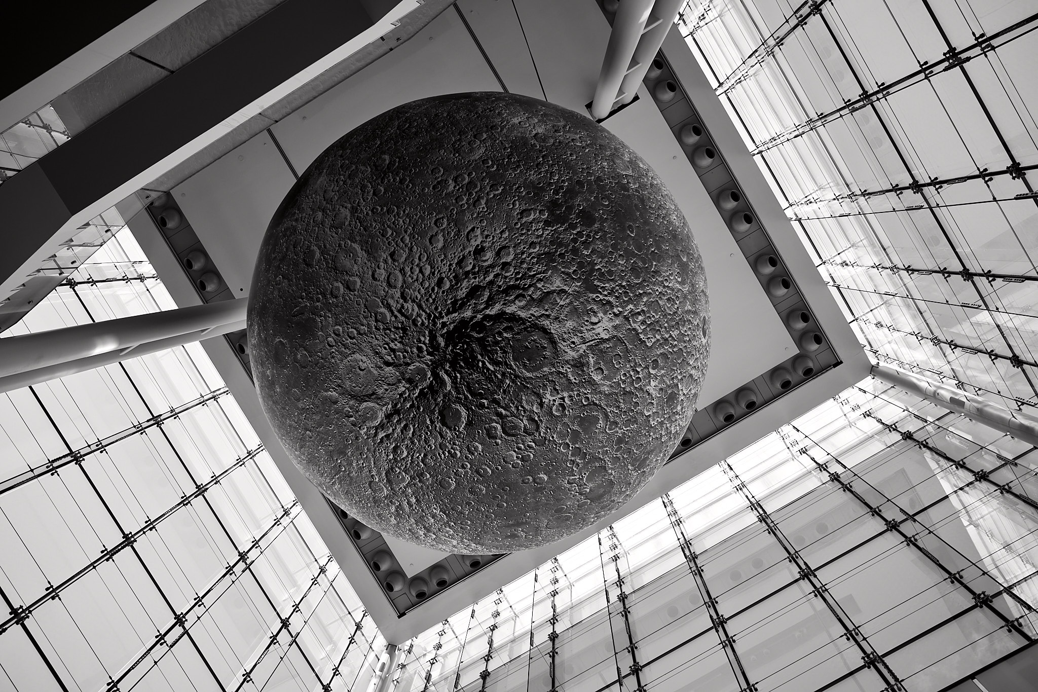 Fujifilm X100V monochrome SDR JPEG of a circular sculpture beneath a geometric glass roof.