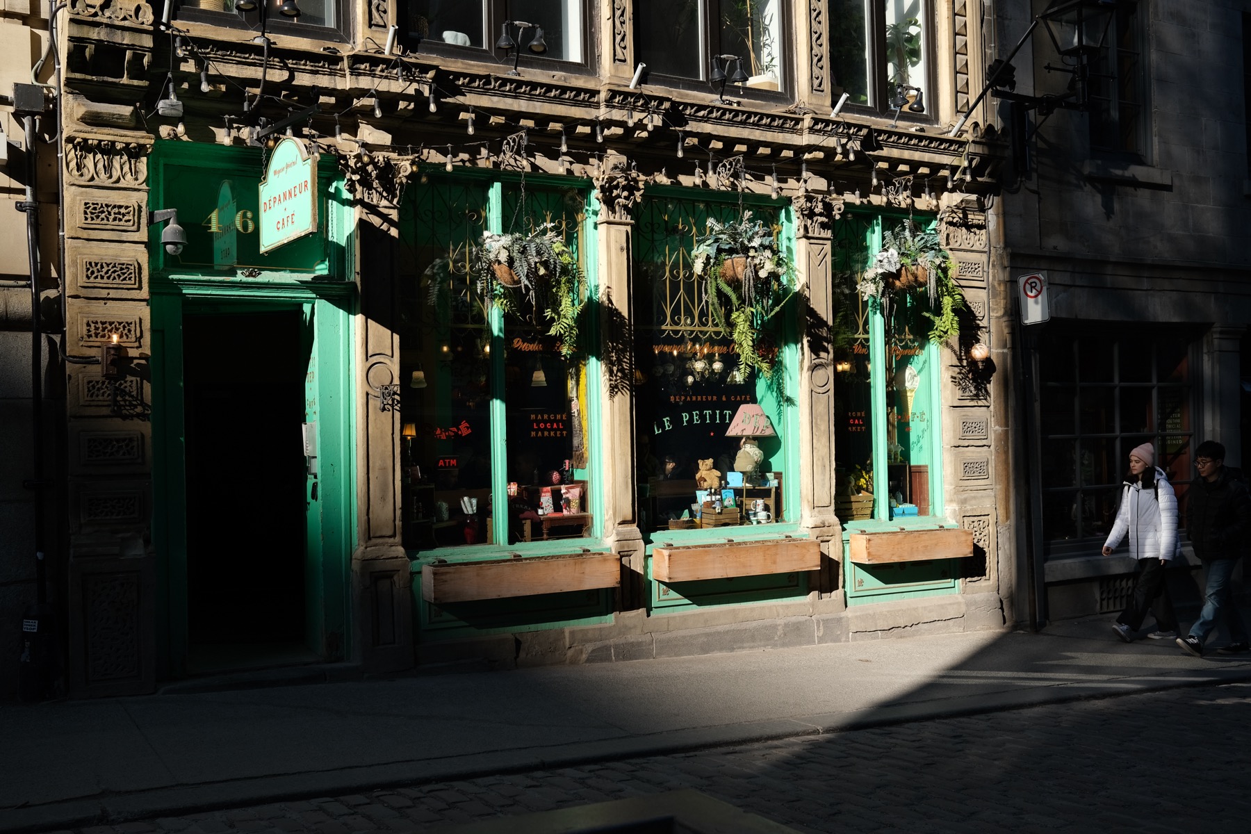 Fujifilm X100V Provia JPEG of a sunlit cafe storefront with teal trim and a hard diagonal shadow.